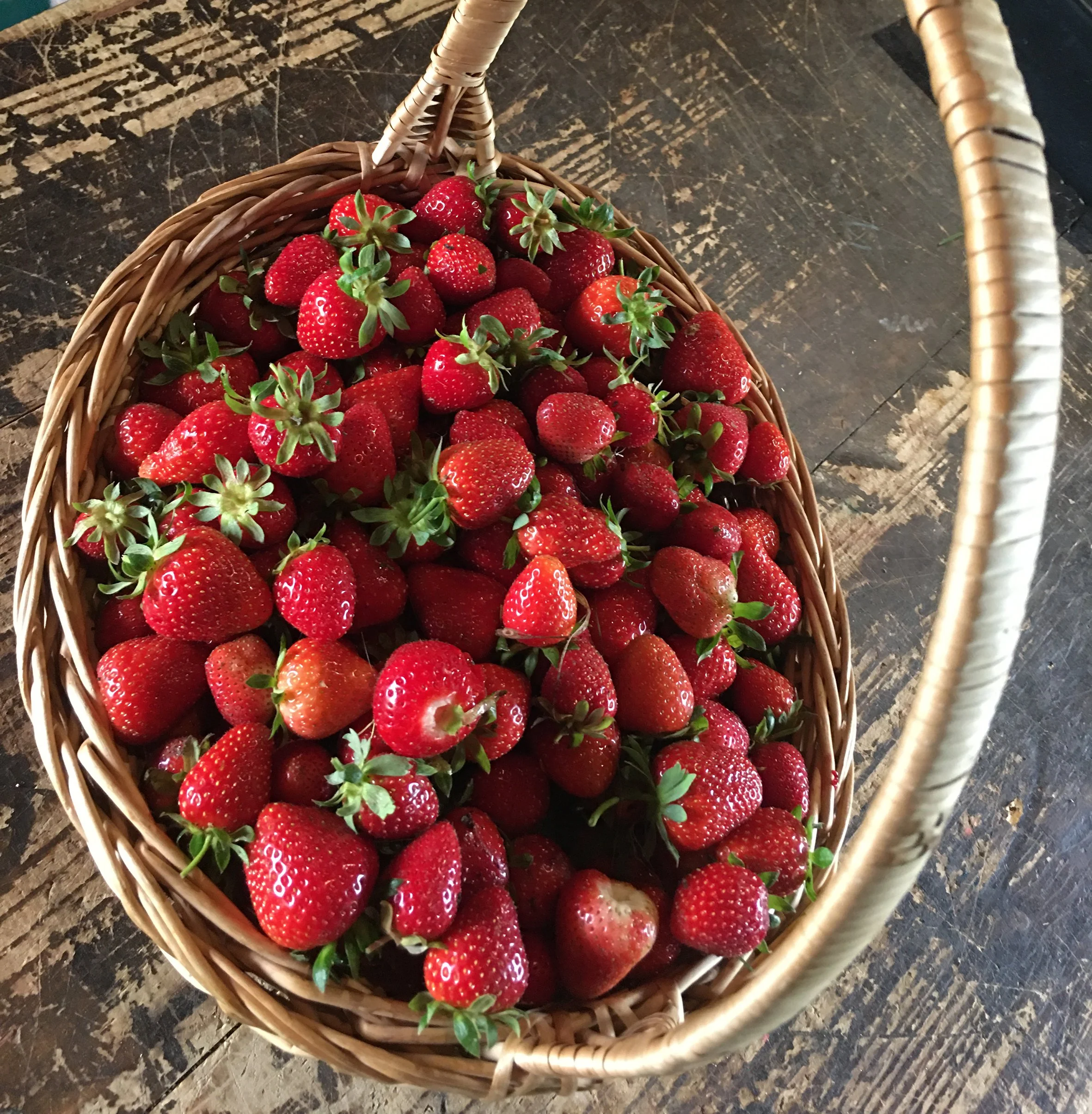Panier en osier rempli de fraises rouges sur une table en bois.