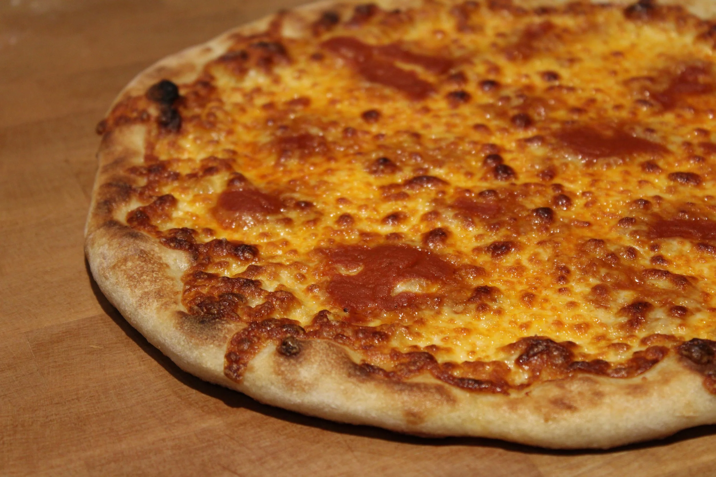 Pizza au fromage avec quelques morceaux de pepperoni sur une surface en bois.