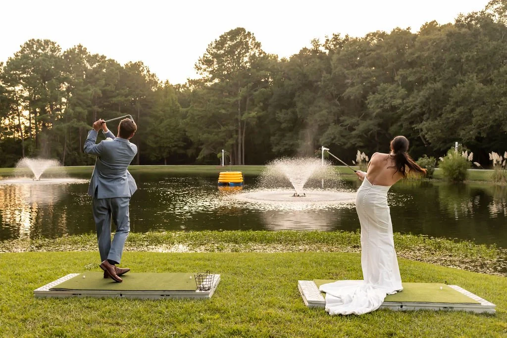 A beach setup for a wedding with white chairs, a white fabric aisle decorated with shells, and an arch draped with white fabric near the water, with palm trees and the ocean in the background.