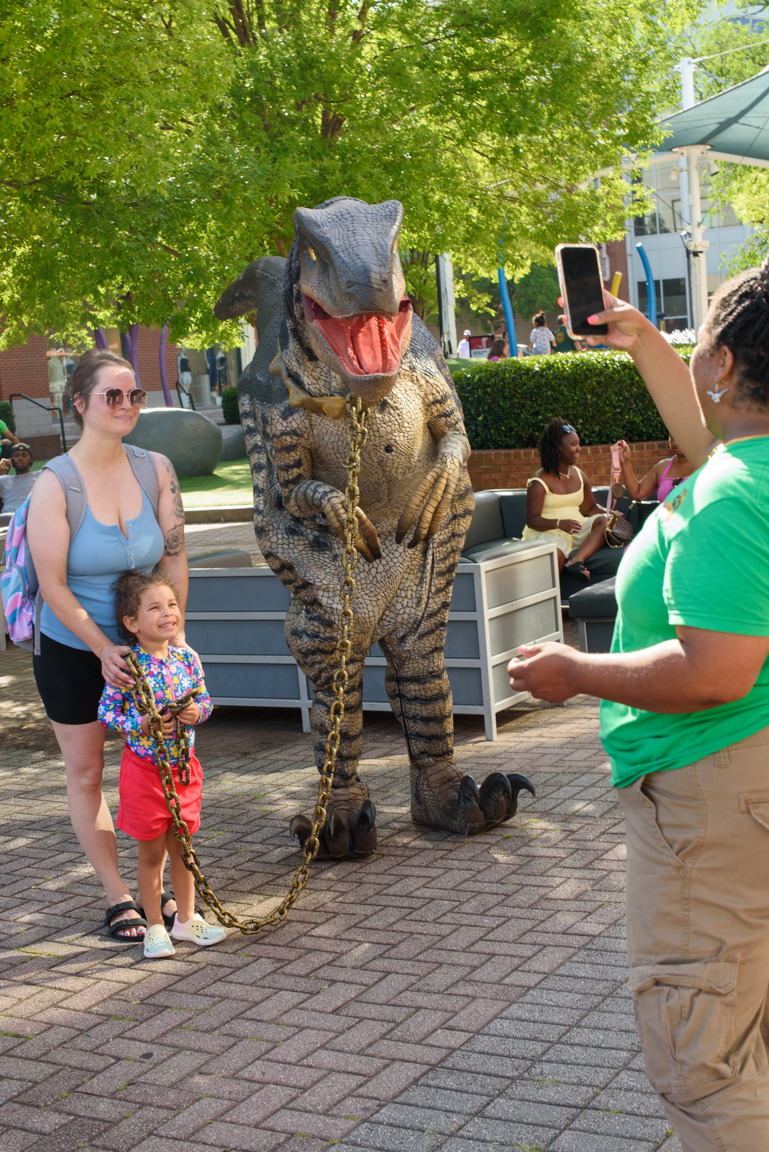 Photo of mother and daughter posing with a costumed dinosaur at an outdoor event