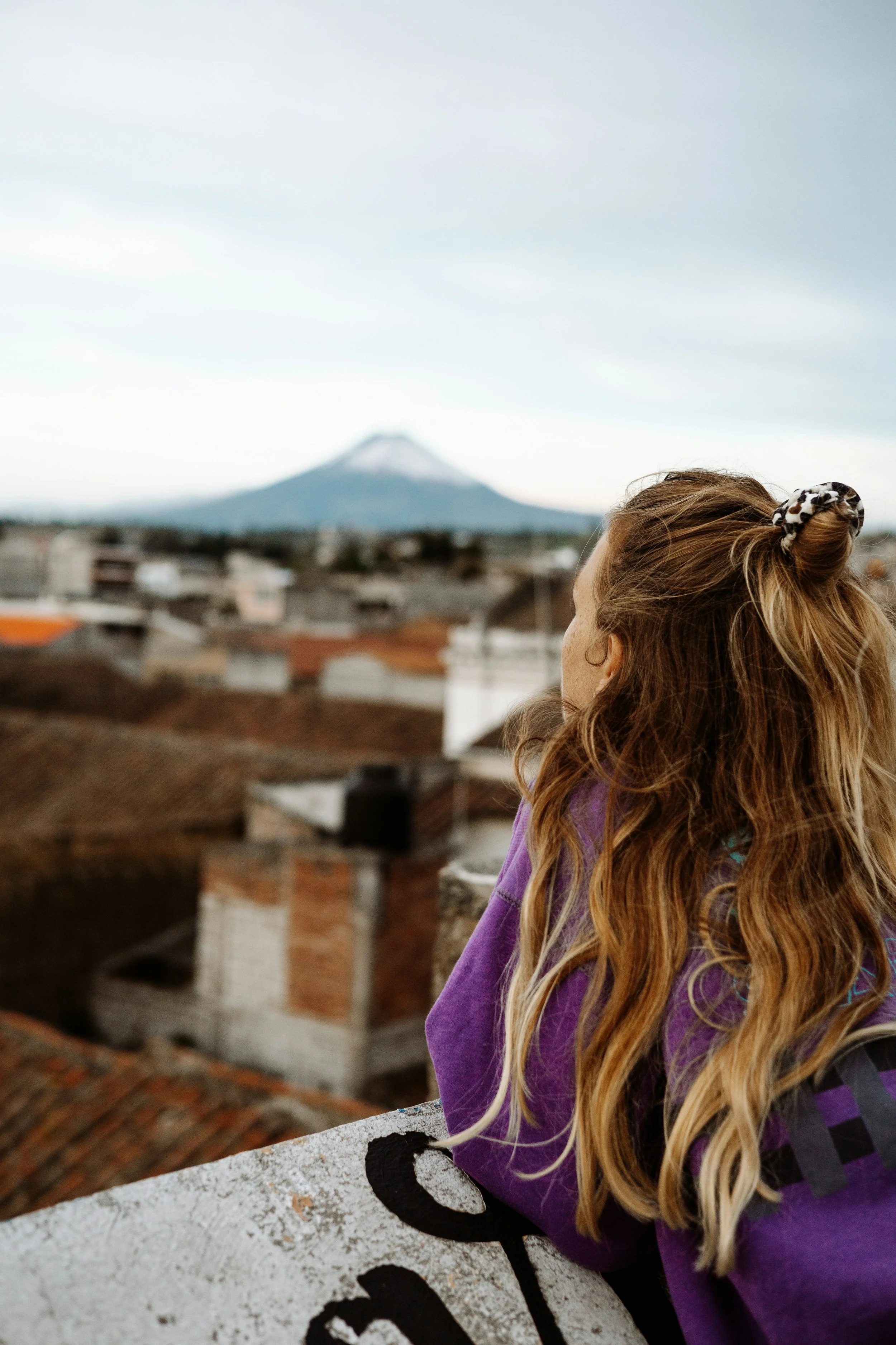 Woman looking out over city rooftops toward a distant volcano in Ecuador