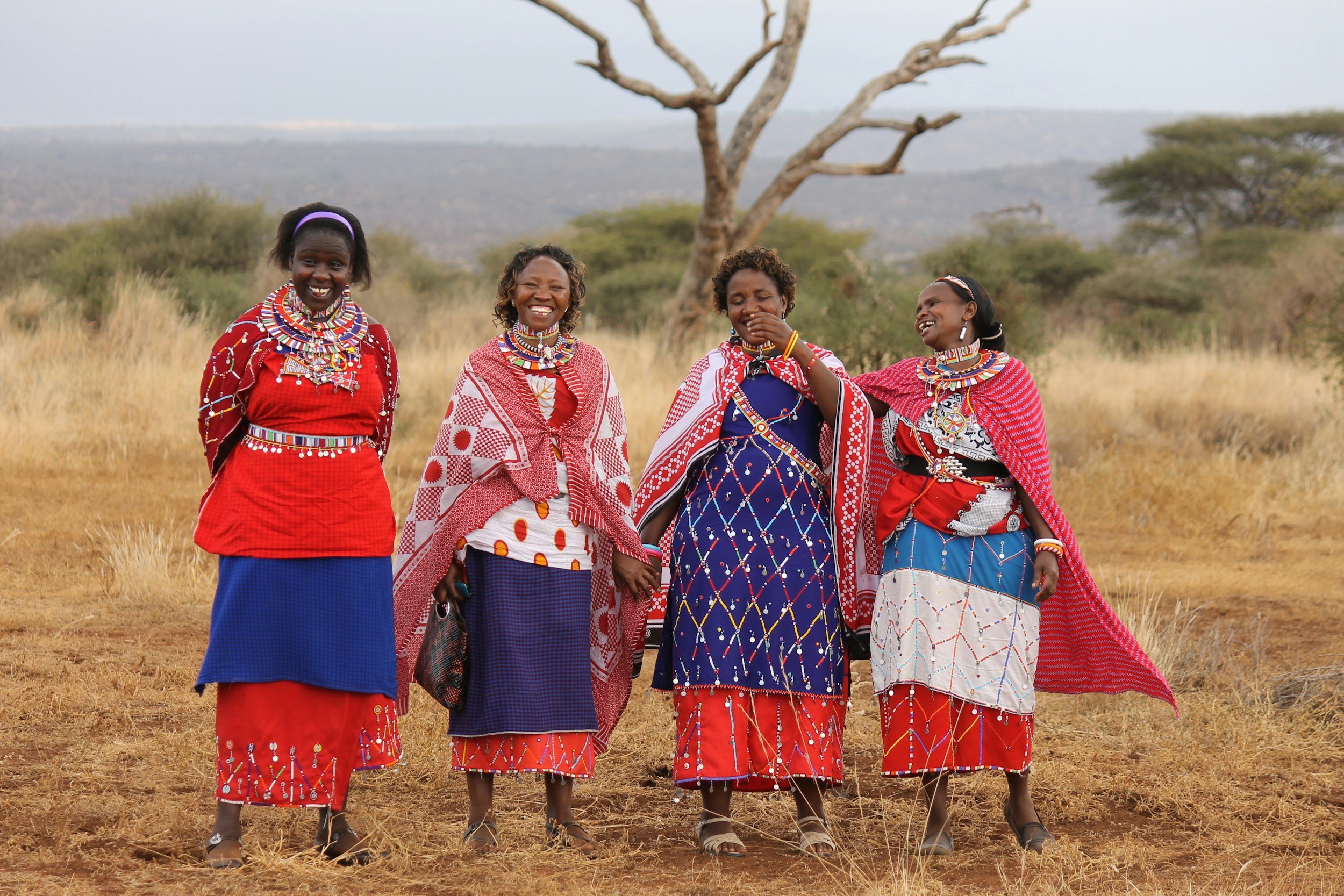 A group of Maasai in colorful traditional dress standing on the savanna.