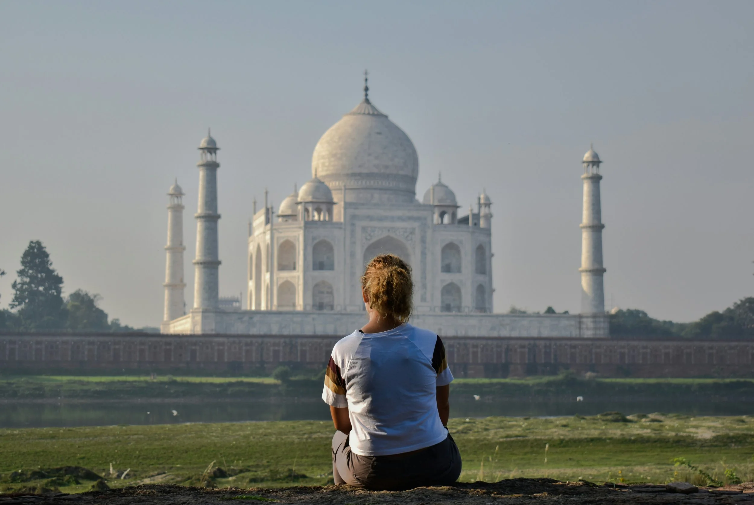 A traveler sitting on the riverbank looking toward the Taj Mahal.