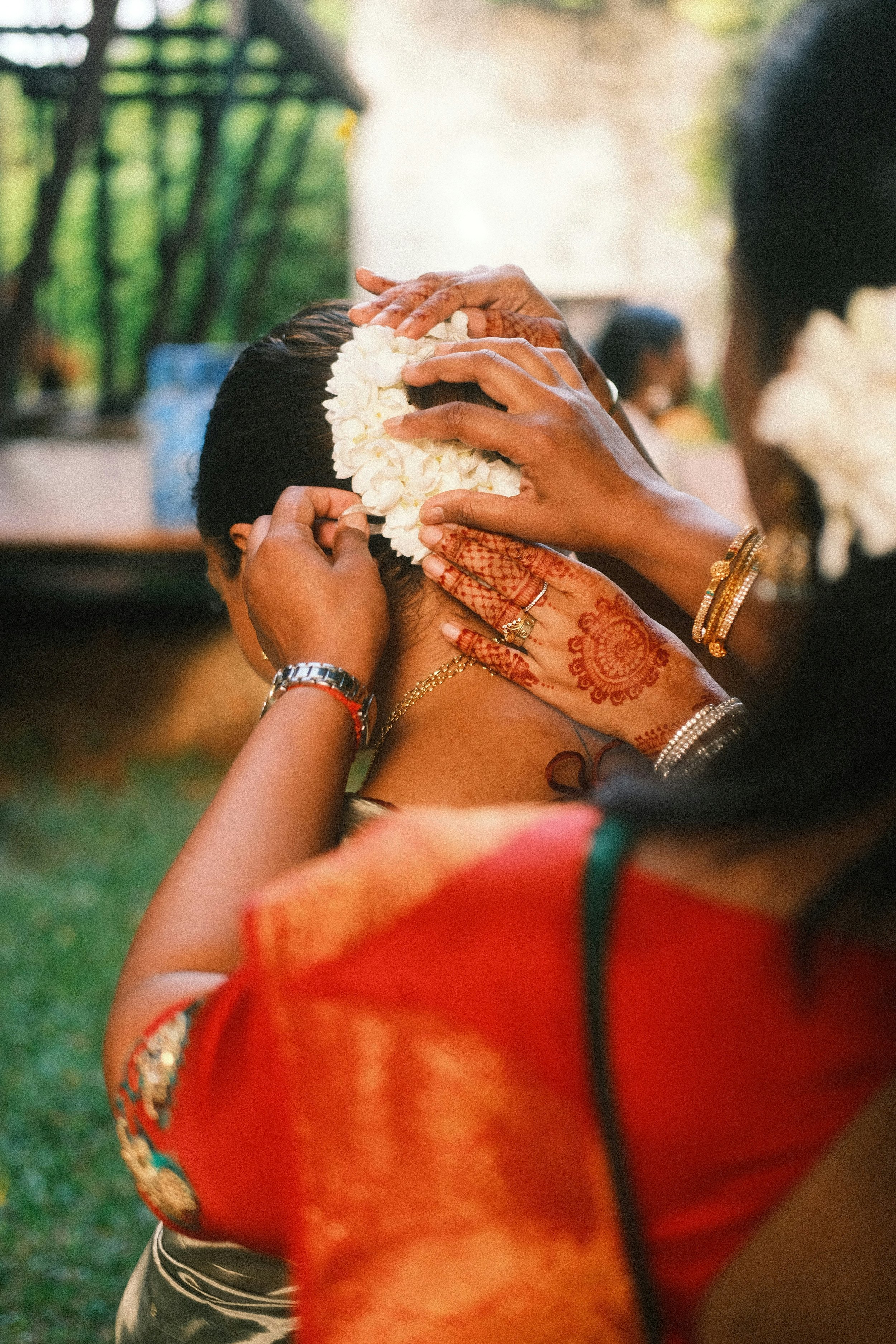 Hands with bangles adjusting a bride's jewelry at an Indian wedding.