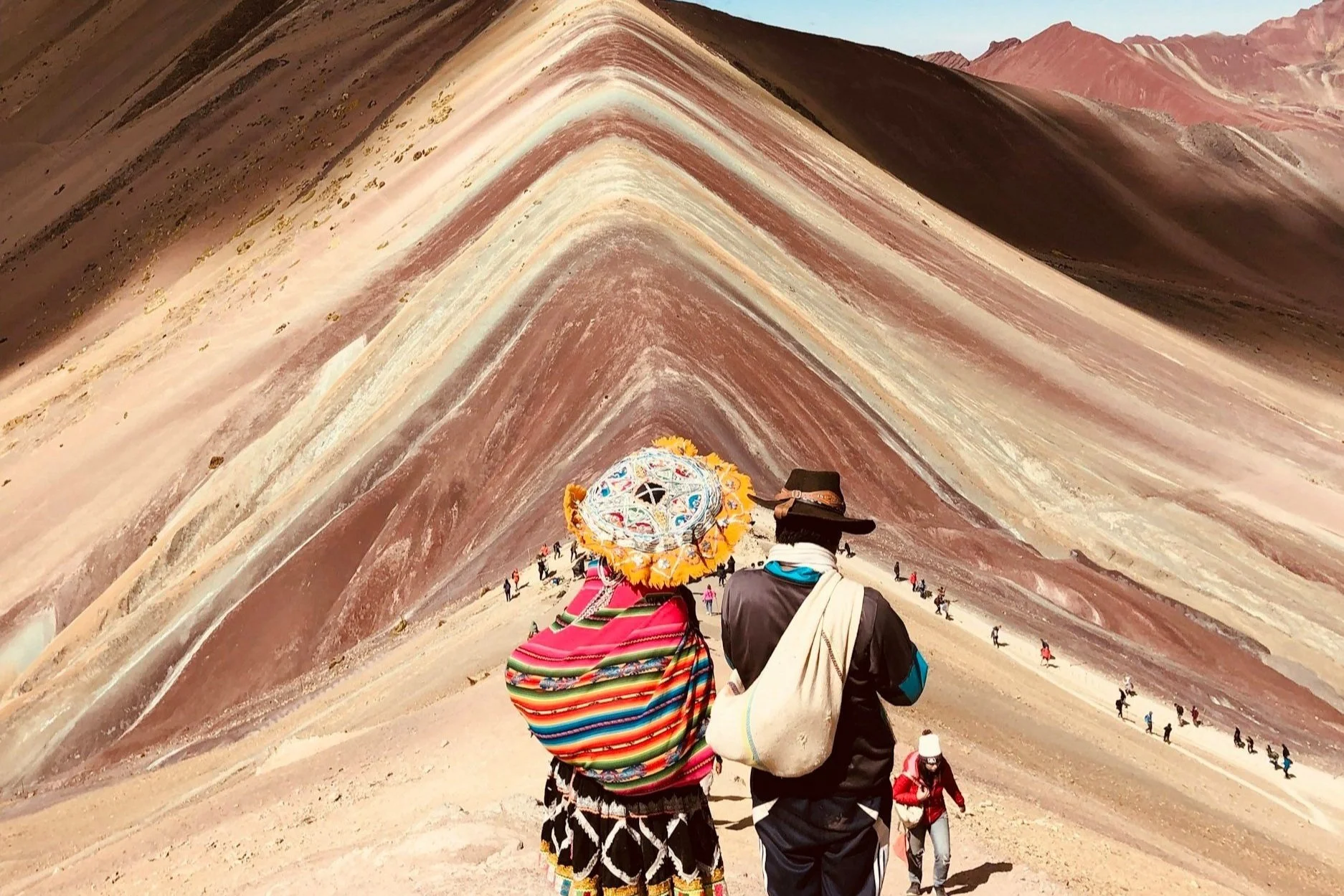 Tourists hike through the colorful Rainbow Mountain with vivid layers of red, yellow, and white in the Andes of Peru.