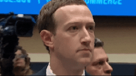 A focused individual at a public hearing or event with microphones and audience in the background.