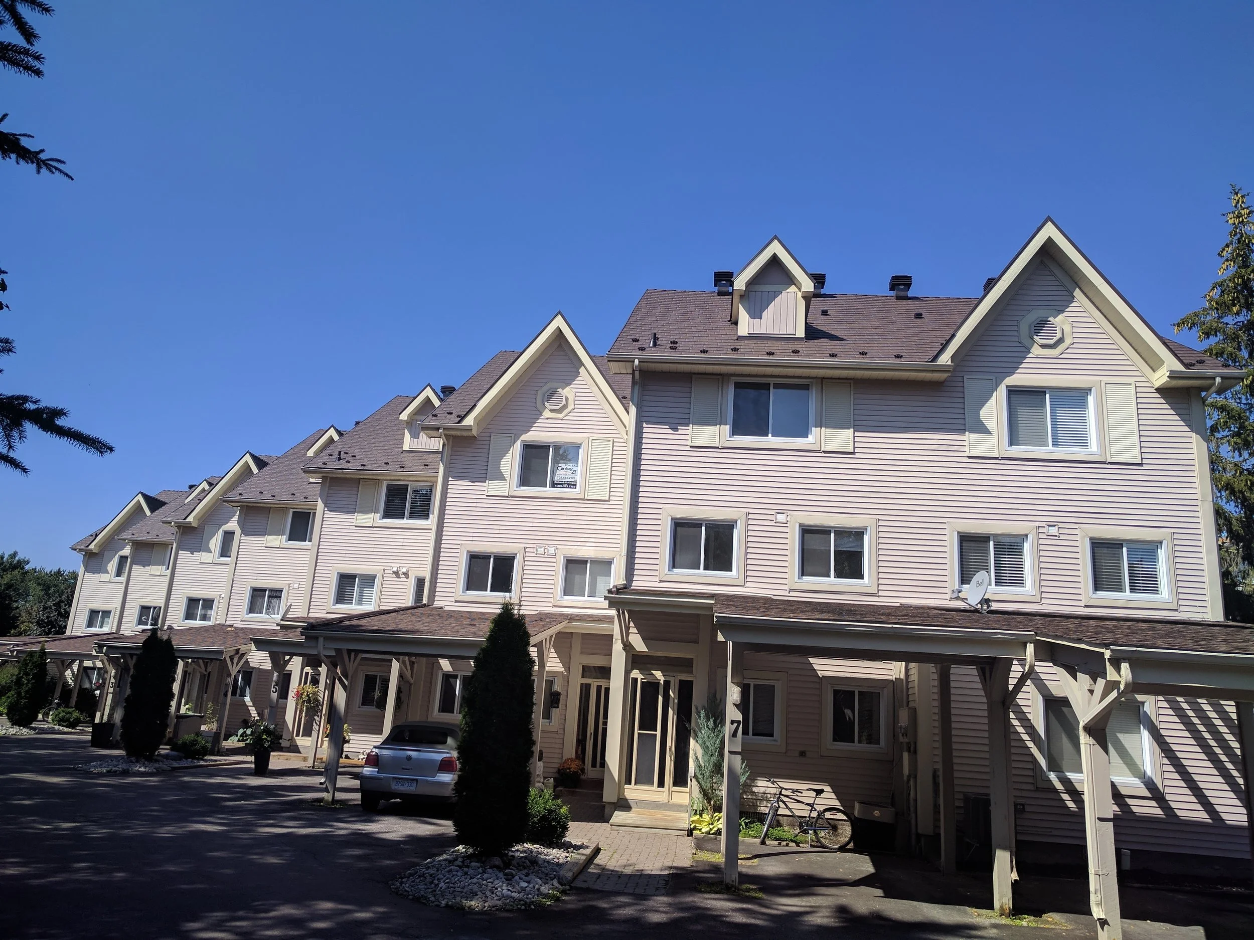 Appartement en rangée avec plusieurs étages, toit en pente, fenêtres, espace de stationnement, arbres et ciel bleu