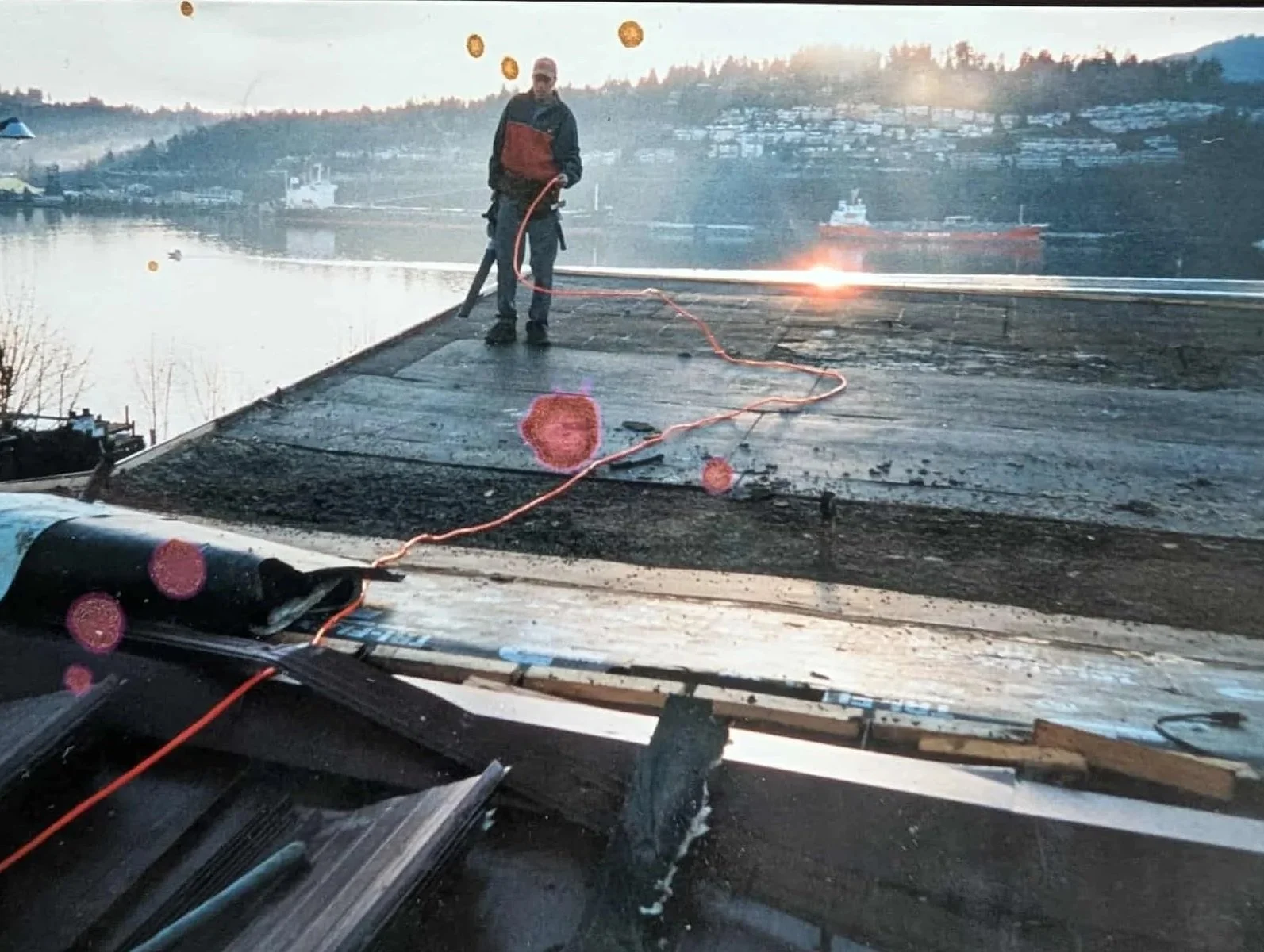 Un ouvrier de construction travaille sur un pont en bois à proximité d'un fleuve, avec des montagnes en arrière-plan, pendant le coucher du soleil.