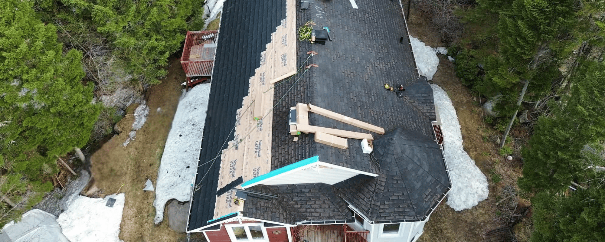 Maison en bois rouge avec une toiture métallique noire Armadura™ en cours d'installation par MetalMax, entourée d'arbres au Québec.