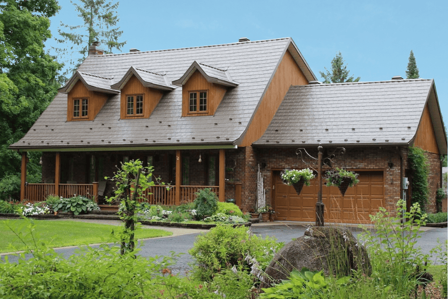 Maison en pierre toiture Armadura avec un toit en tuiles, fenêtres en bois, et un garage, entourée d'un jardin verdoyant.
