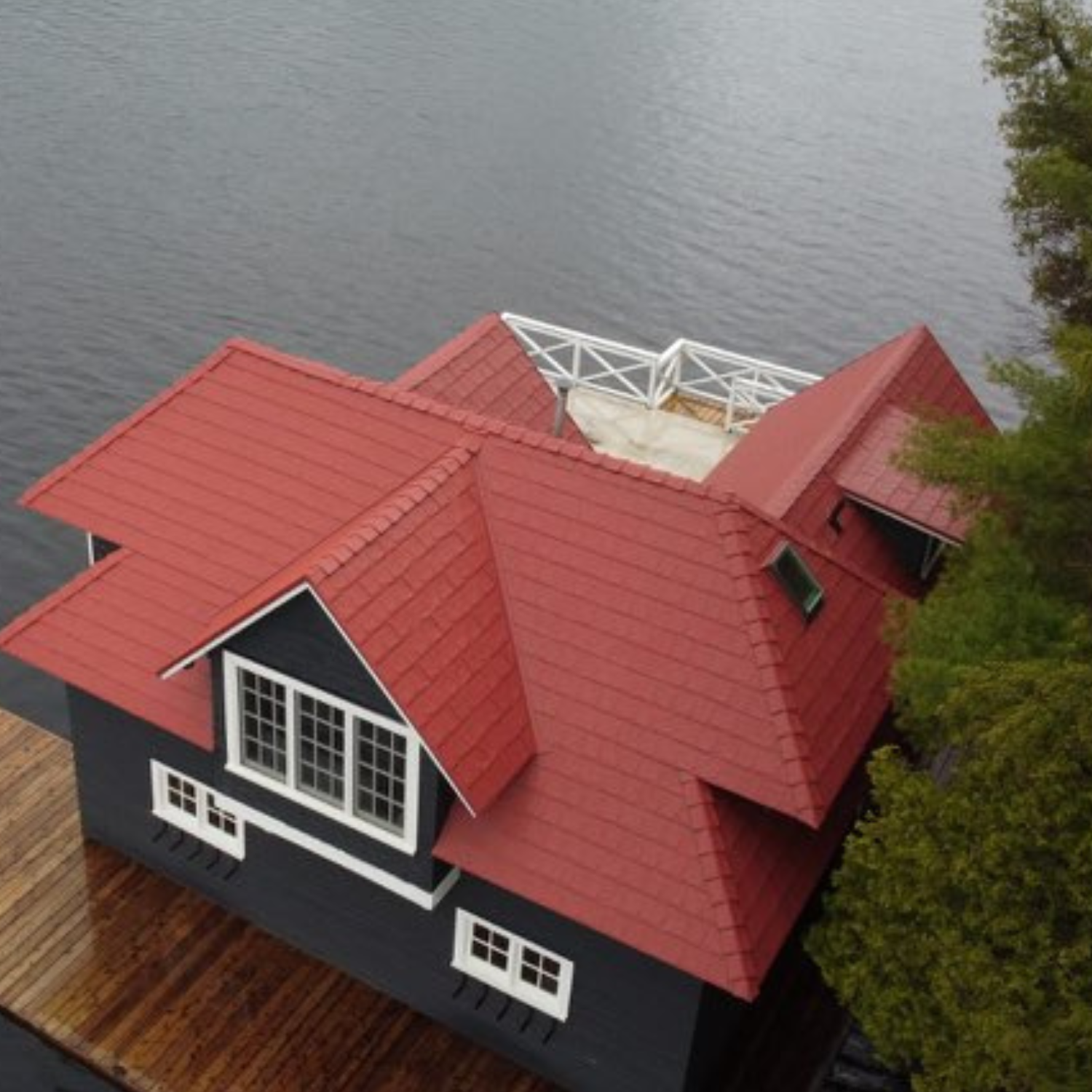 Une maison avec toit rouge située au bord d'un plan d'eau, vue aérienne.