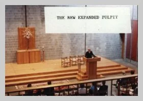 a photo - taken above from the choir loft - of the chancel. a caption reads "the new expanded pulpit"