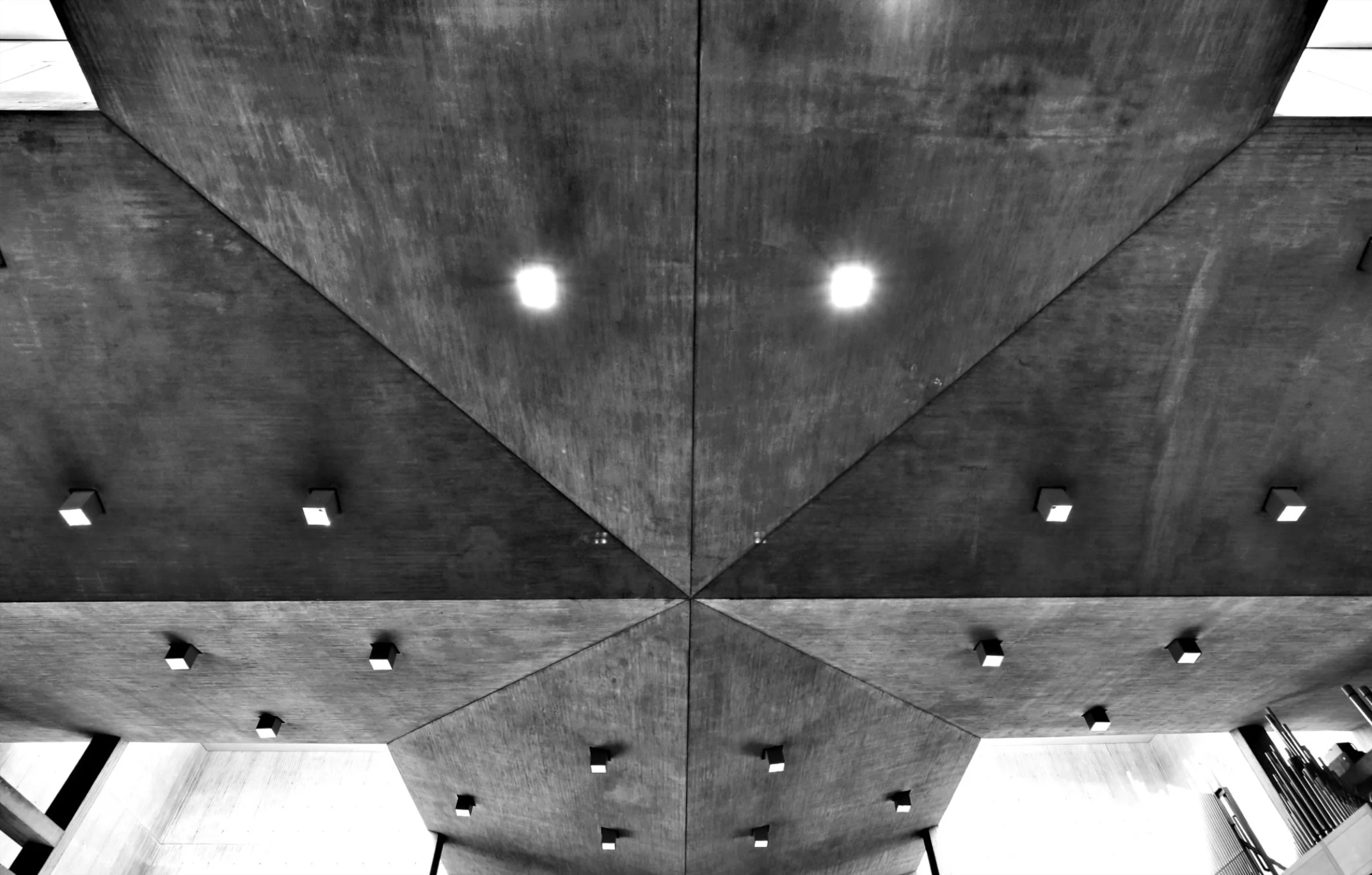 A black and white photograph of a modern ceiling with geometric design, featuring square ceiling lights arranged in a grid pattern.