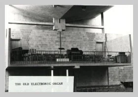 a black and white photo of the choir loft before the current pipe organ was installed.  a caption reads "the old electronic organ"