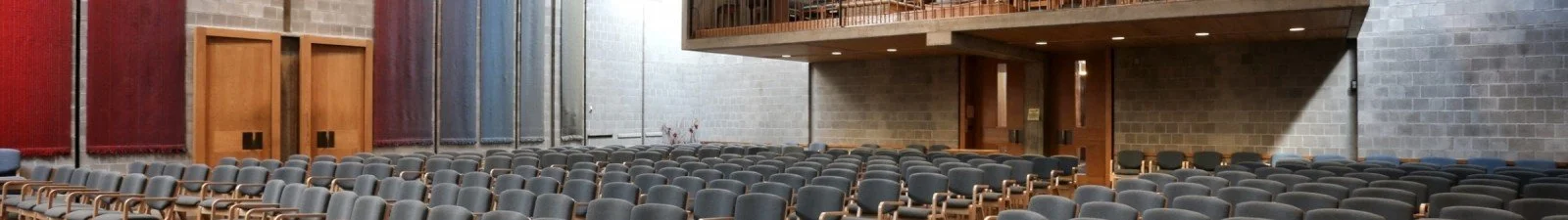 Empty auditorium with rows of gray theater seats, brick walls, and wooden panels.