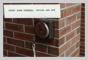 a brick wall with a round electronic metal button with a wheelchair user embossed in blue. a caption reads "front door openers, inside and out"