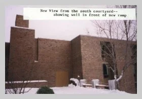 a photo of the exterior South side of the building featuring a snow-covered patio. a caption reads "new view of the south courtyard - showing wall in front of new ramp"