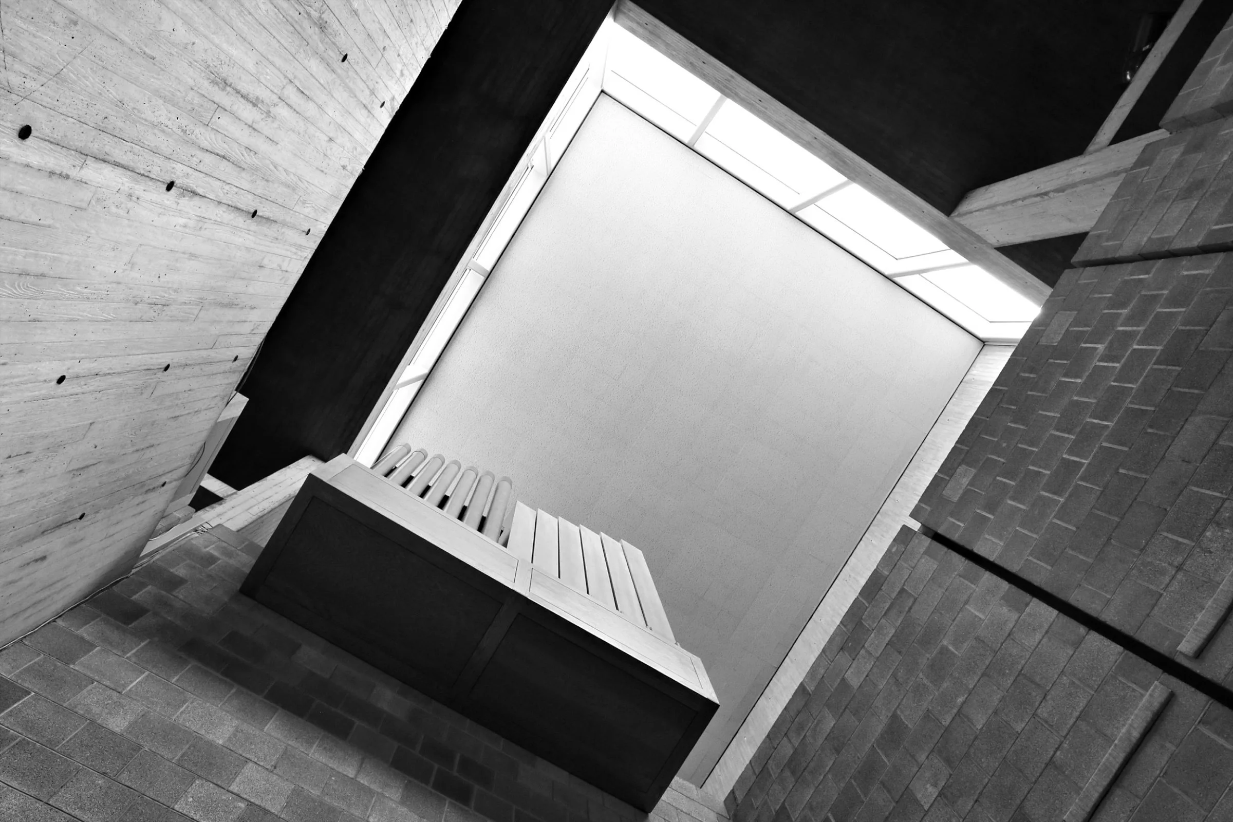 Interior view of a modern building with angular ceiling, large windows, brick walls, and wooden accents in black and white.