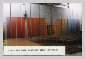 a photo of the chancel taken from stage right showing the wall and showcasing the rainbow gradient of the woven wall hangings. a caption reads "after the wall hangings were installed"
