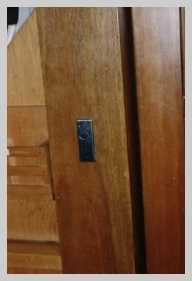 a photo of an interior wall with a vertical, silver button embossed with a wheelchair user in blue.