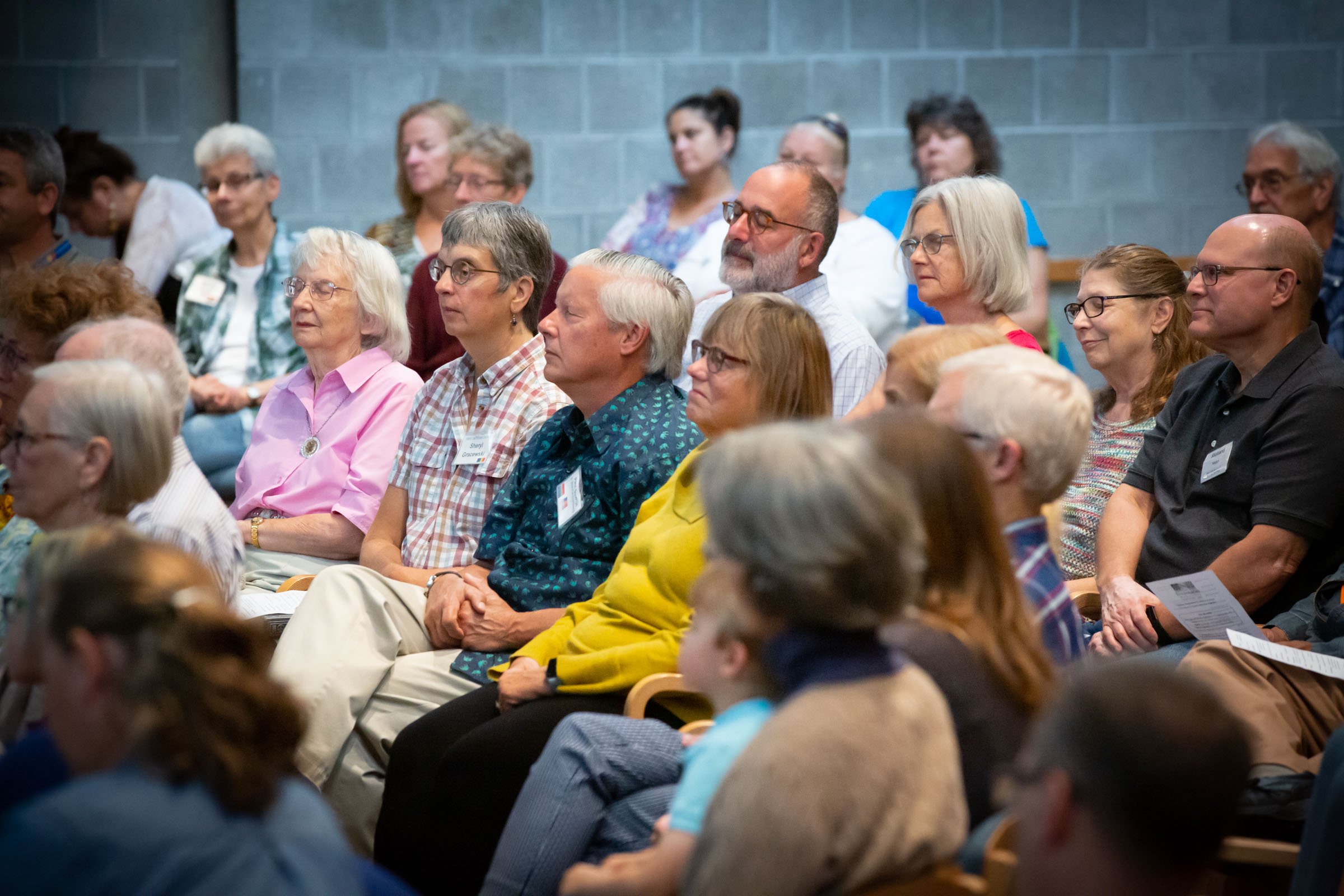 Audience of diverse adults attentively listening at an indoor event or conference.