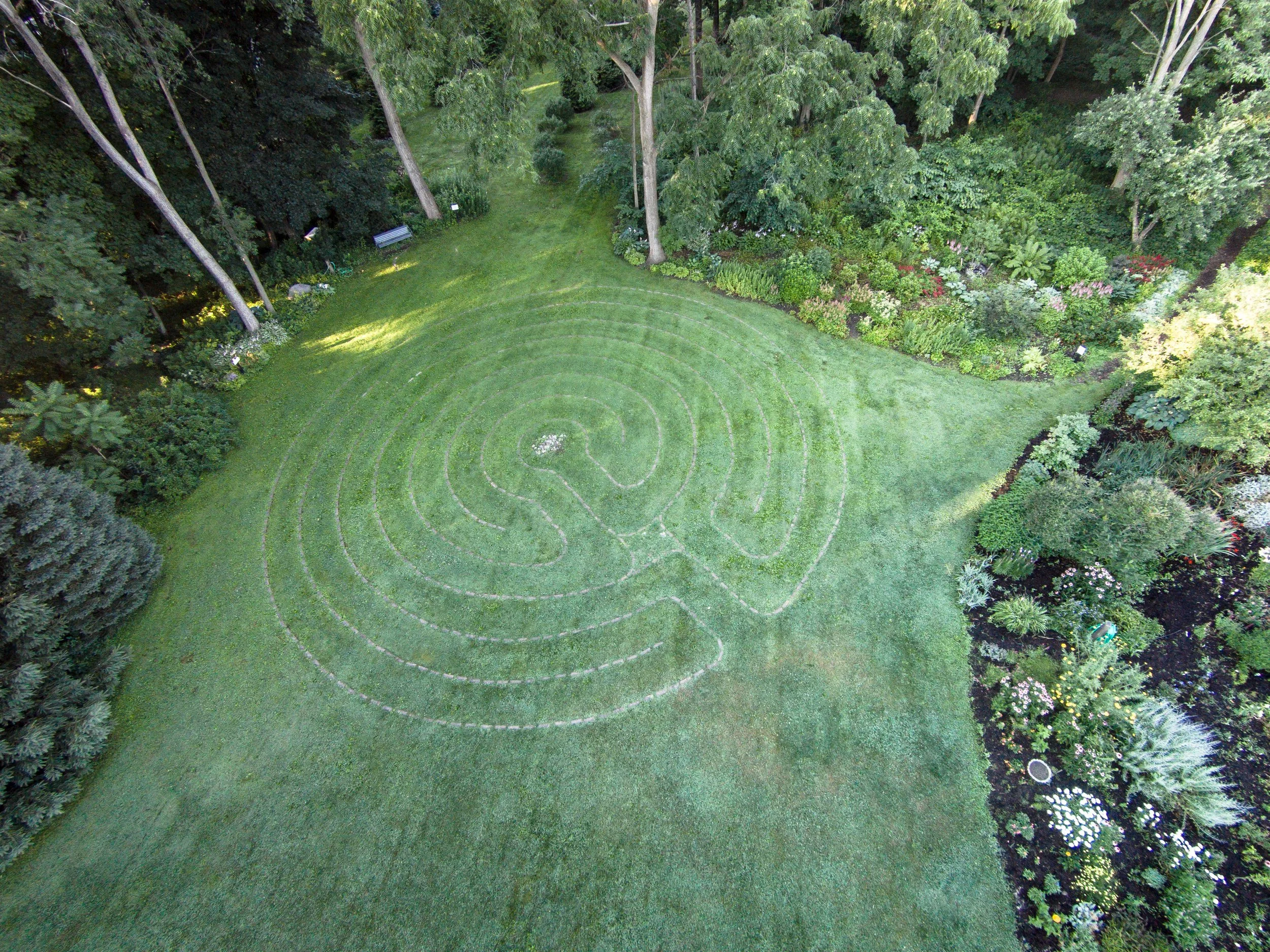 Aerial view of a garden with a large grassy area, flower beds, and tall trees surrounding the space.