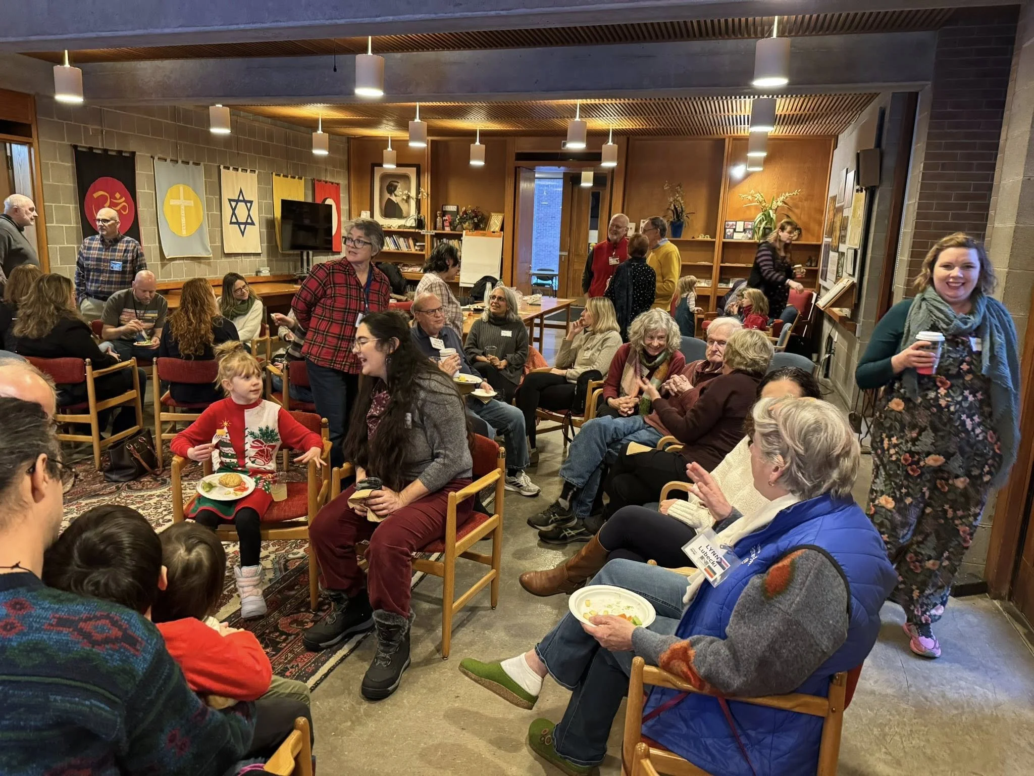 Adults and children gather in a church lounge for conversation and food during a community gathering.