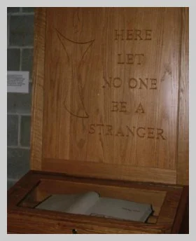 a photo of a wooden plaque that reads "here let no one be a stranger" that hangs above a glass-enclosed book of members signatures