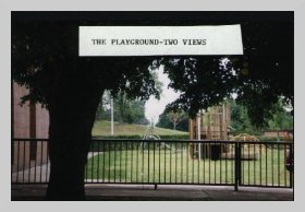 a photo taken from under a tree of a fenced-in area with a caption that reads "the playground - two views"