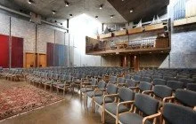 Empty auditorium with rows of chairs and a stage, featuring brick walls and modern architectural design.