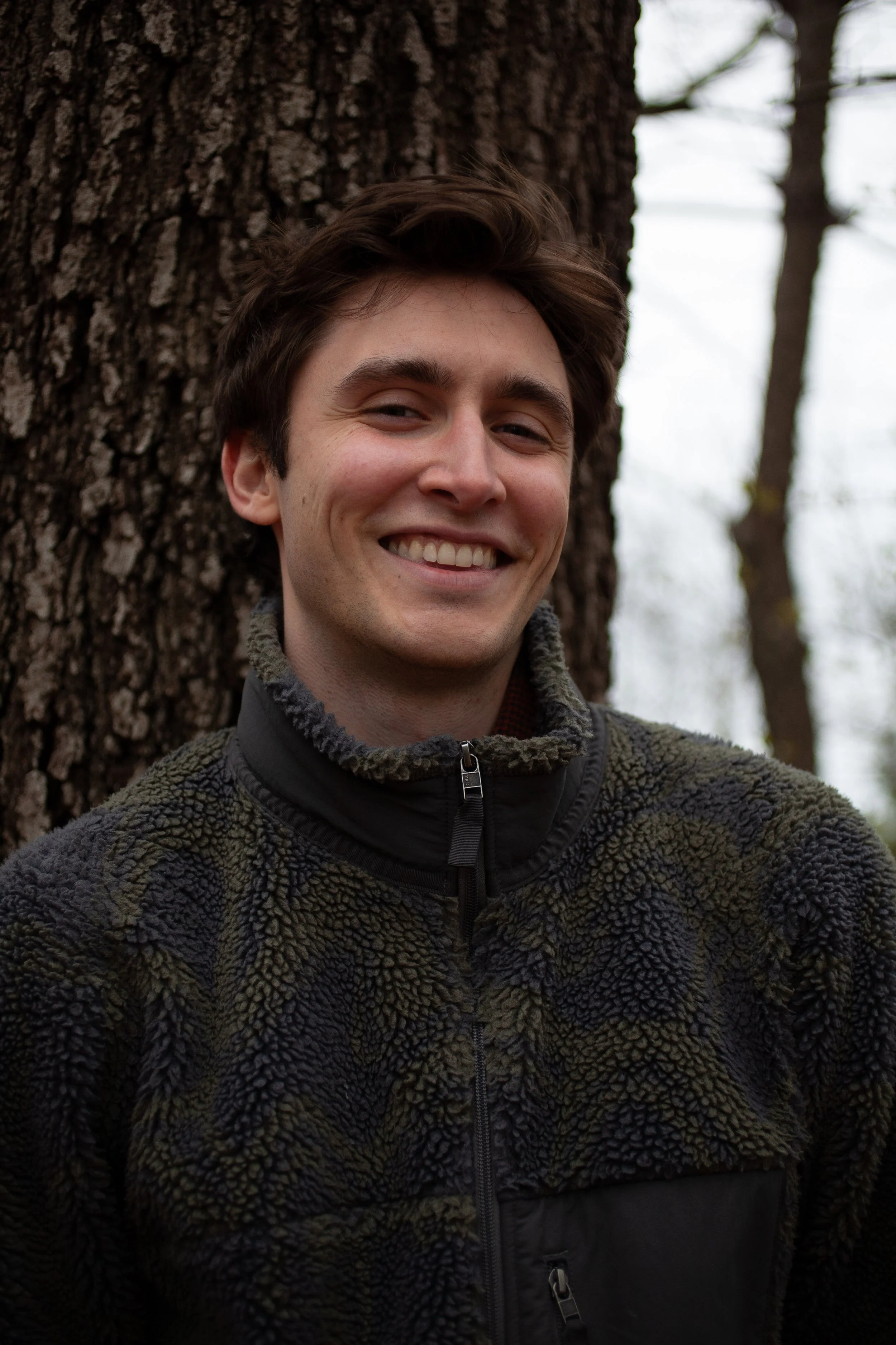 Person smiling in front of a tree wearing a dark fleece jacket