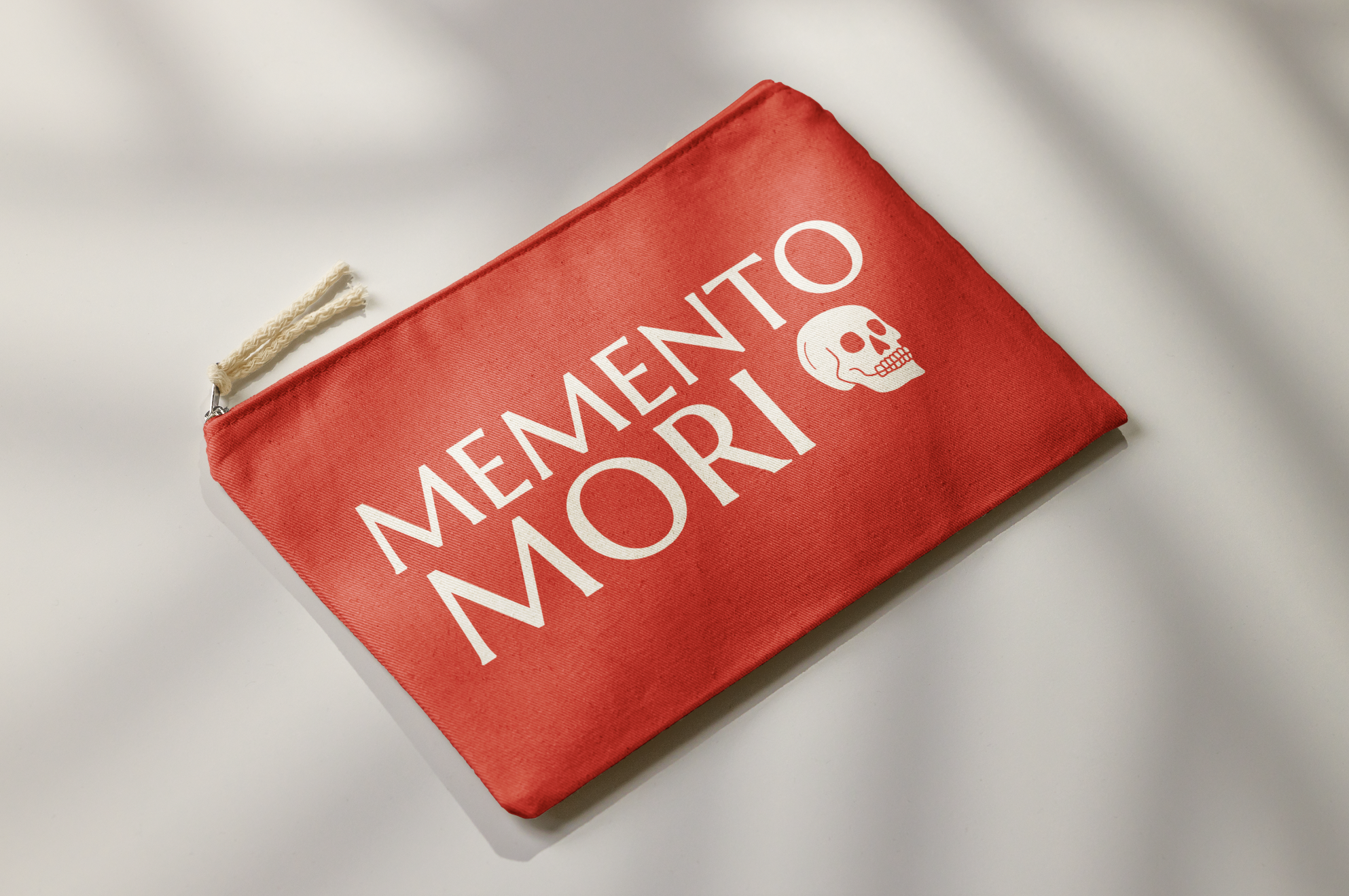 A red pouch with white text saying 'MENENTO MORTI' and a skull graphic in the center, placed on a white surface.