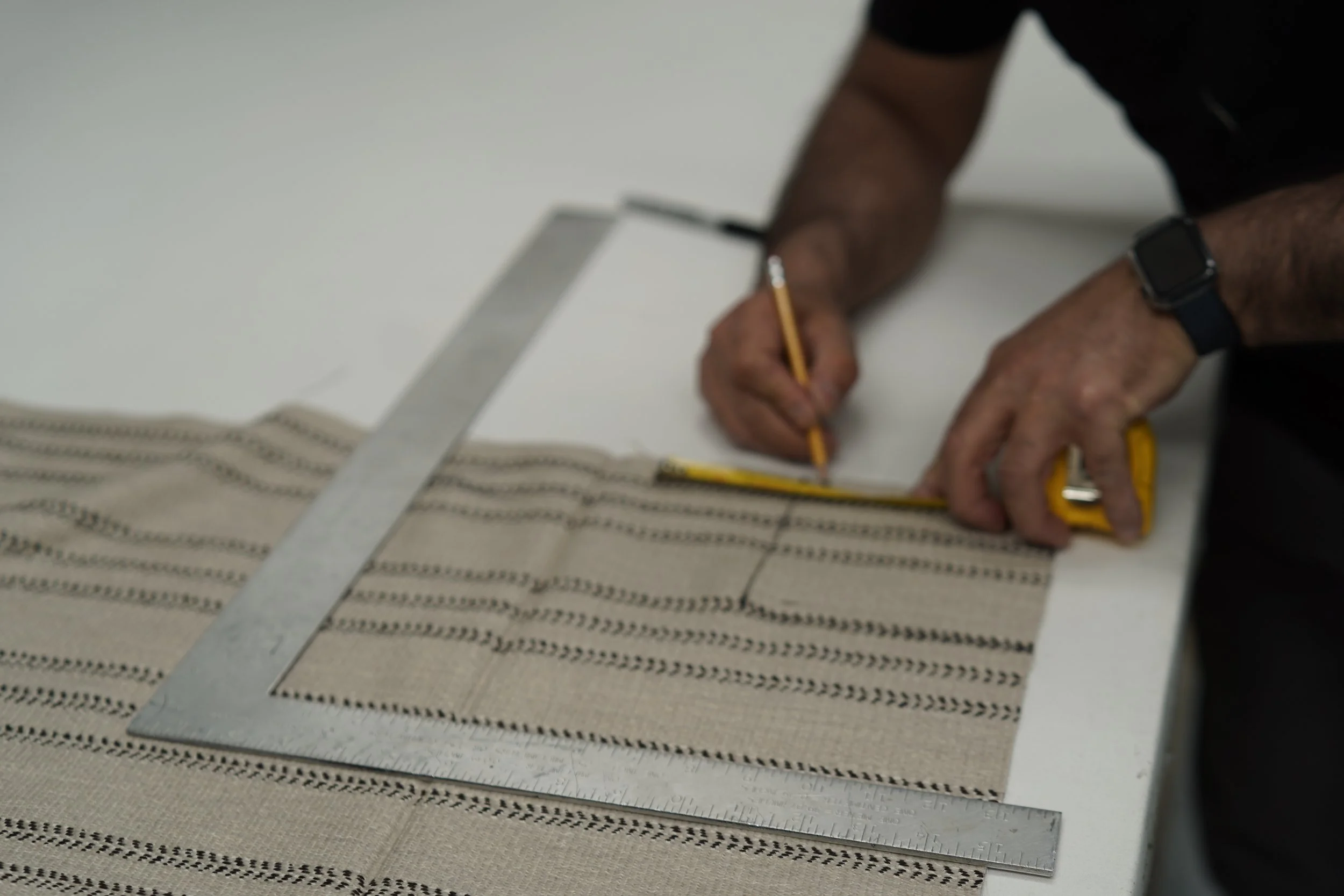 Person marking measurements on a striped fabric pattern with a ruler and pencil.