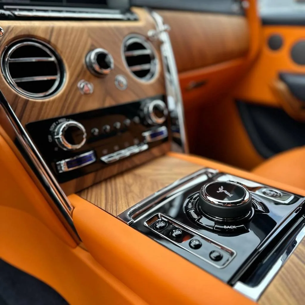 Interiores de un coche de lujo con panel de control y cambios en acabado de madera y detalles en negro y cromado, con asientos y puertas en color naranja.