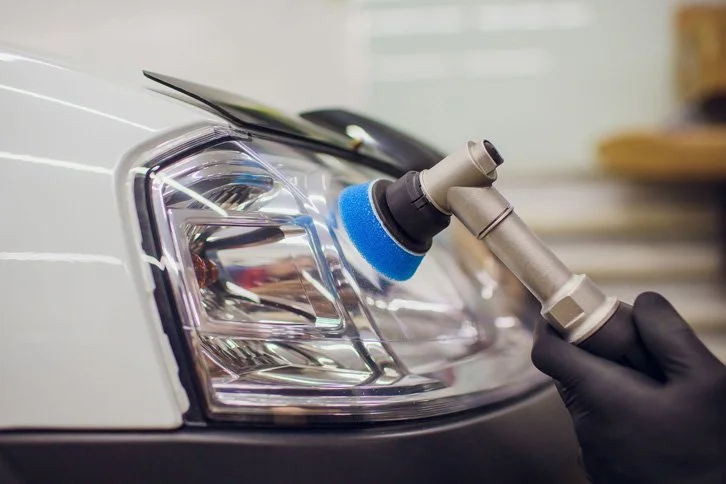 Una mano con guante negro utilizando un pistón de limpieza para faro de automóvil.