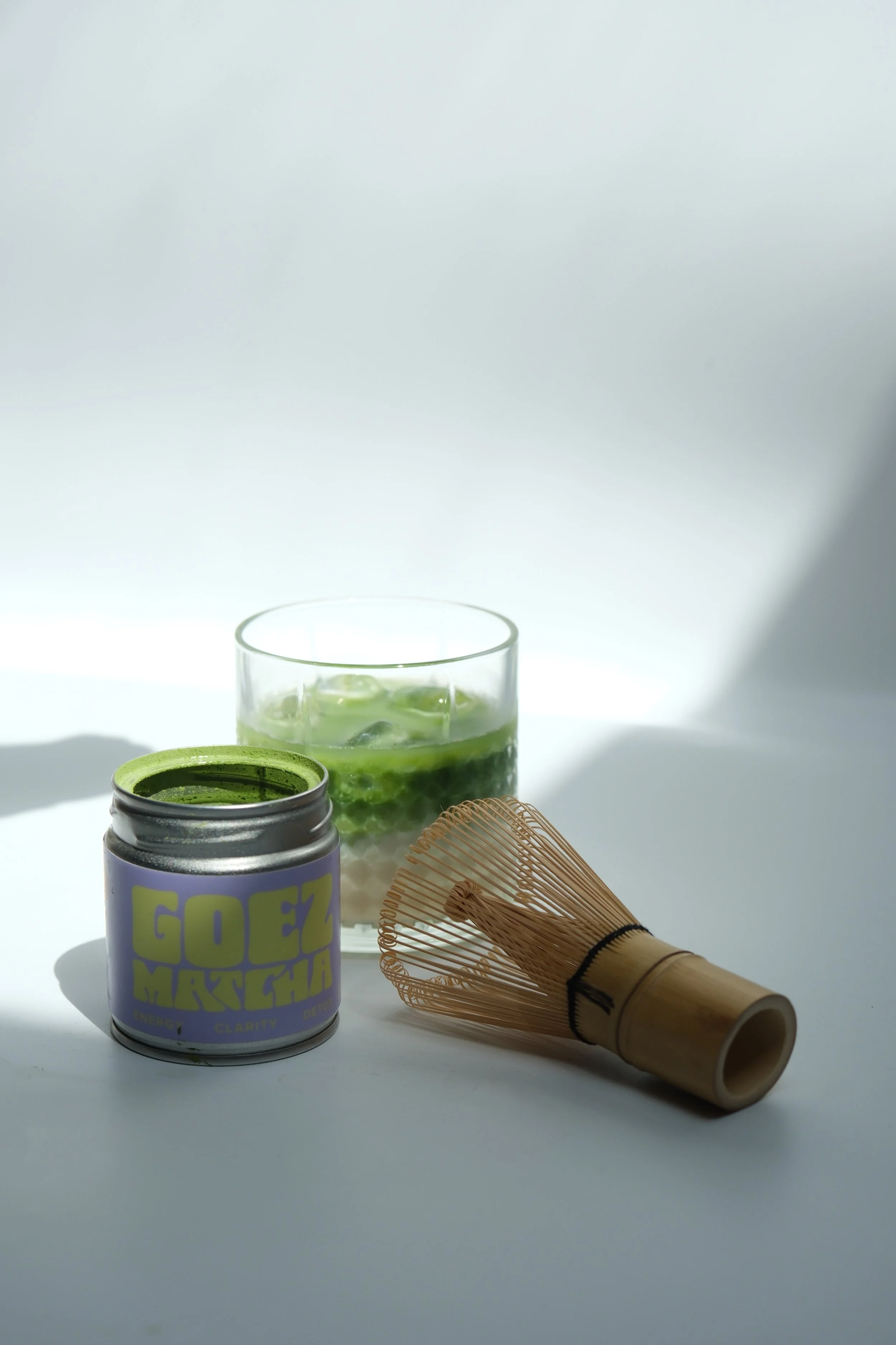 Matcha powder container, bamboo whisk, and glass with green drink