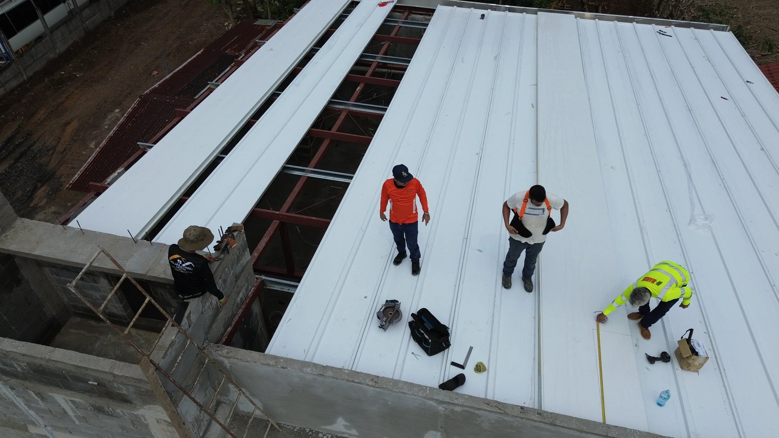 Cuatro trabajadores en una construcción de techo, instalando láminas metálicas blancas en un edificio en construcción.