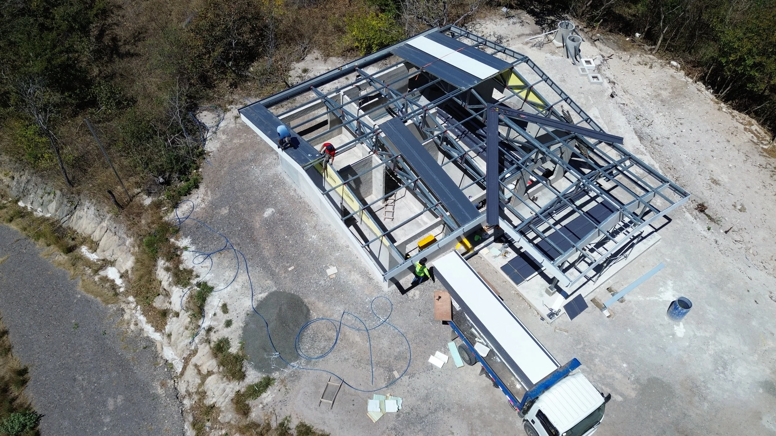 Construcción de una estructura metálica en un sitio al aire libre, con trabajadores ensamblando las partes y materiales de construcción alrededor.