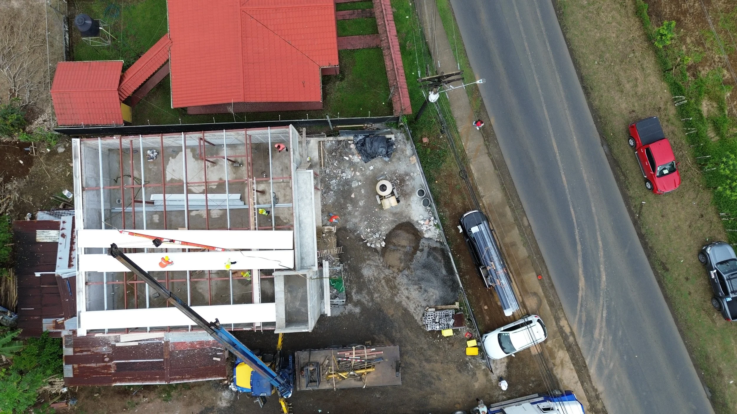Construcción de un edificio desde una vista aérea, con trabajadores en la estructura y maquinaria en el sitio.