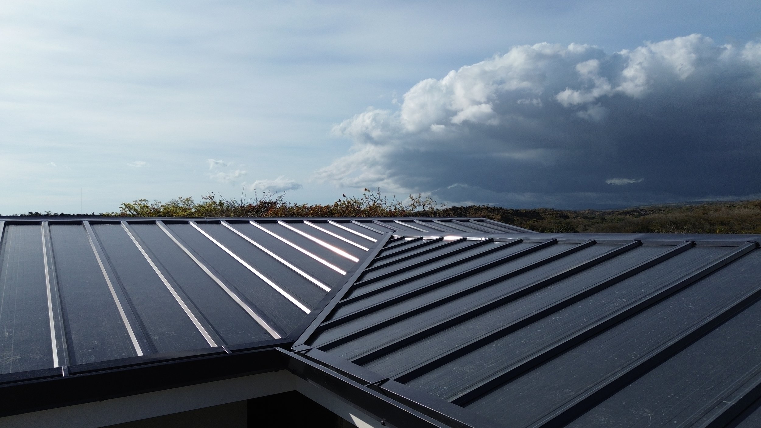 Techo de metal con paneles solares en un día nublado, con árboles en el fondo y un cielo con nubes.