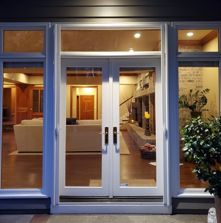 Wide retractable screen door highlighting a cozy living room featuring a beige sofa, wooden flooring, stone fireplace, potted plants, and warm lighting.