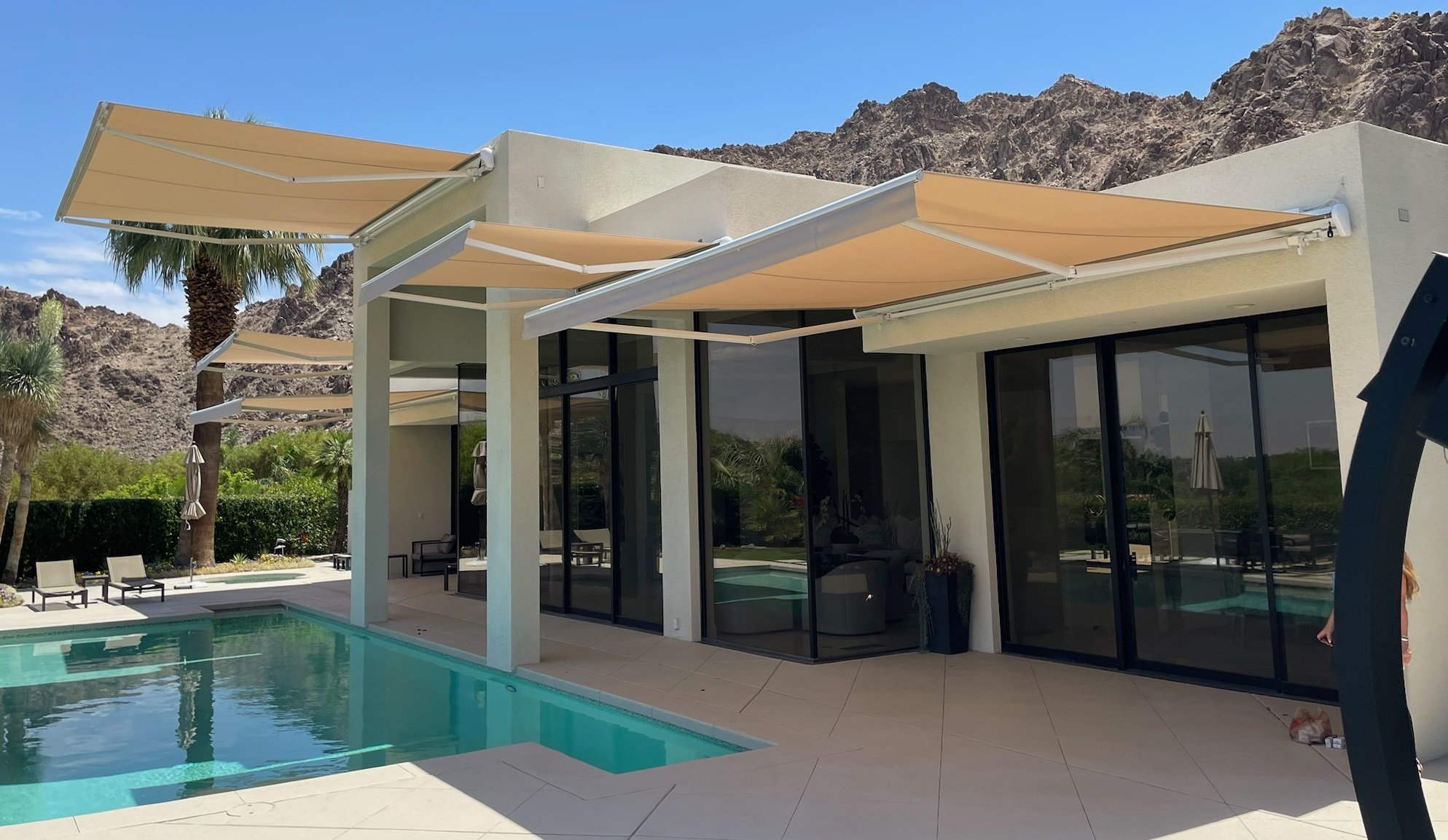 Motorized retractable awning shading a modern house with a swimming pool.