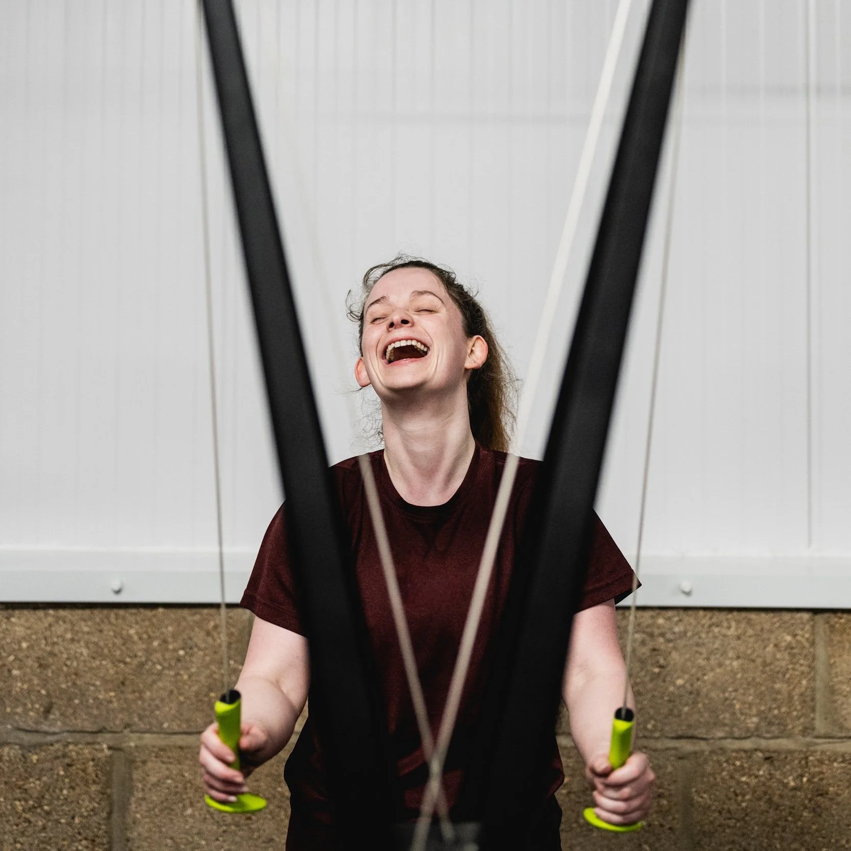 An Ovrload member smiling and laughing while using a ski erg against a white wall.