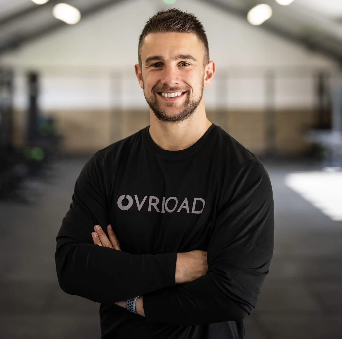 Ovrload Director Mike, standing in the gym smiling at the camera, arms crossed.