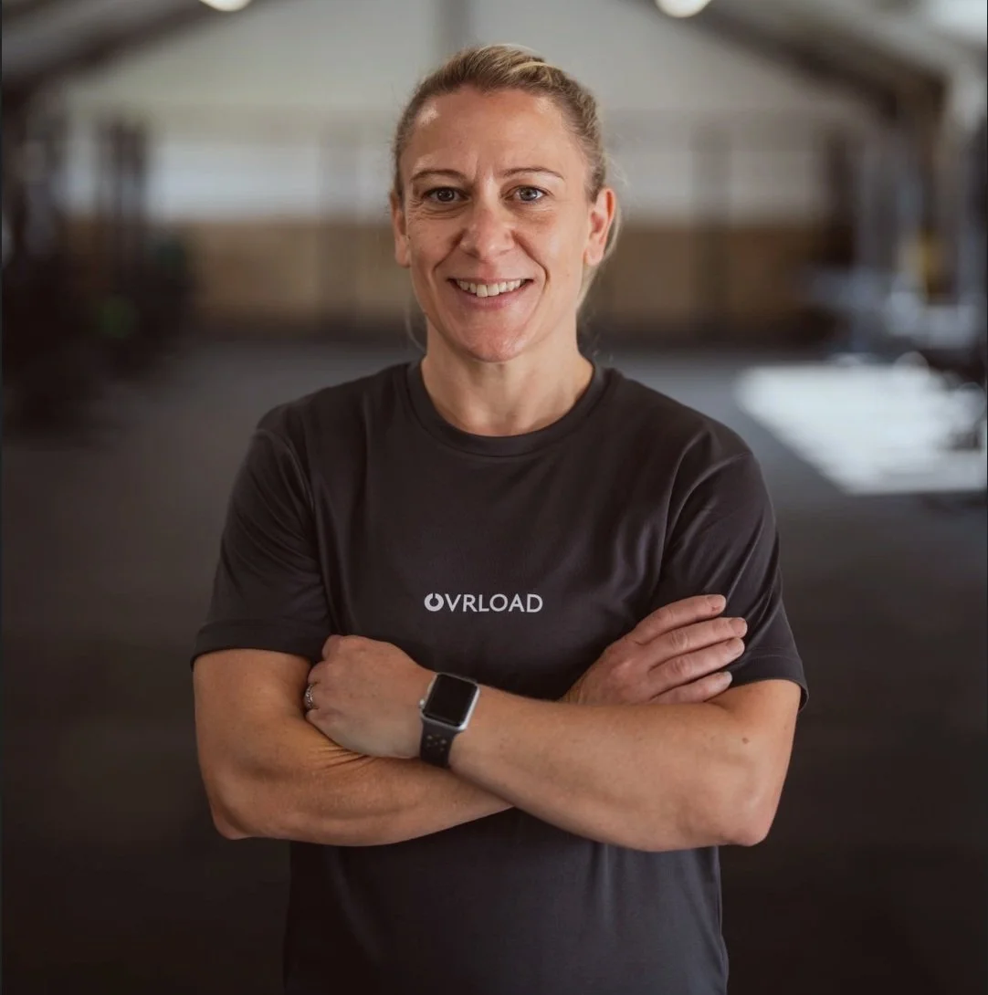 Ovrload coach Kelly, standing in the gym, smiling with arms crossed.