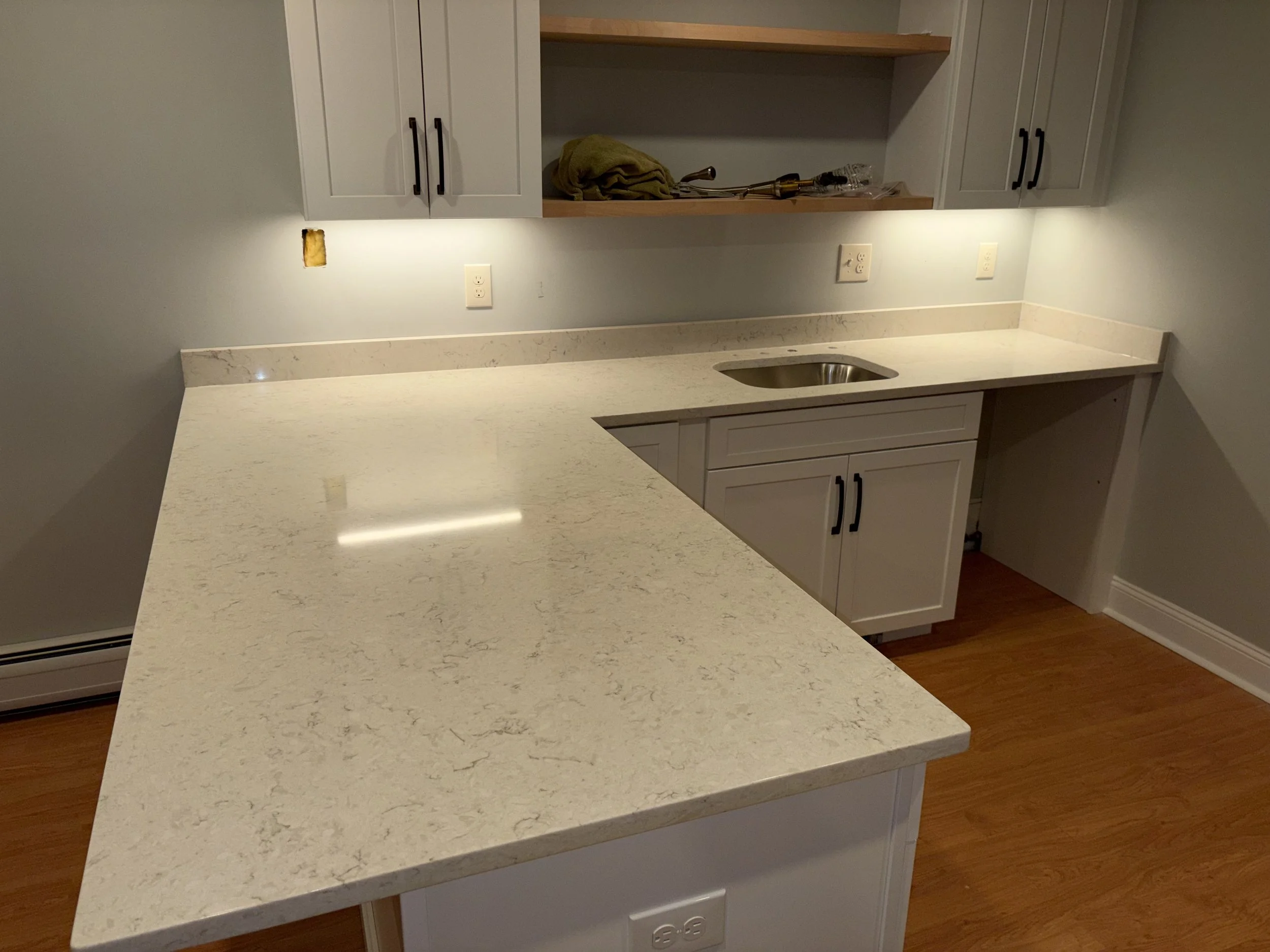 Kitchen with white cabinets, marble countertop, and small sink, with open shelving and electrical outlets.