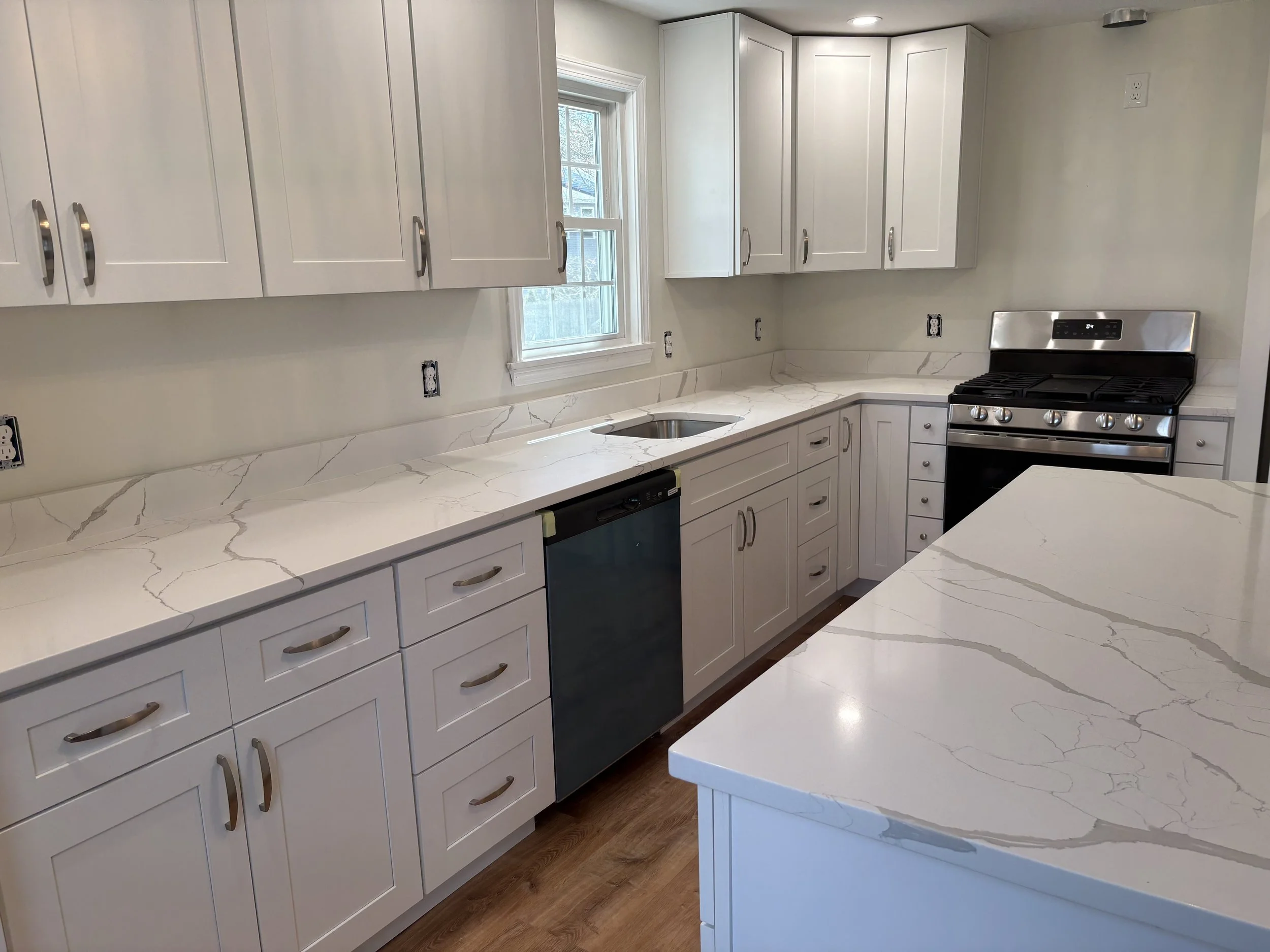 Kitchen with white cabinets, marble countertop, stainless steel stove, and sink under a window.