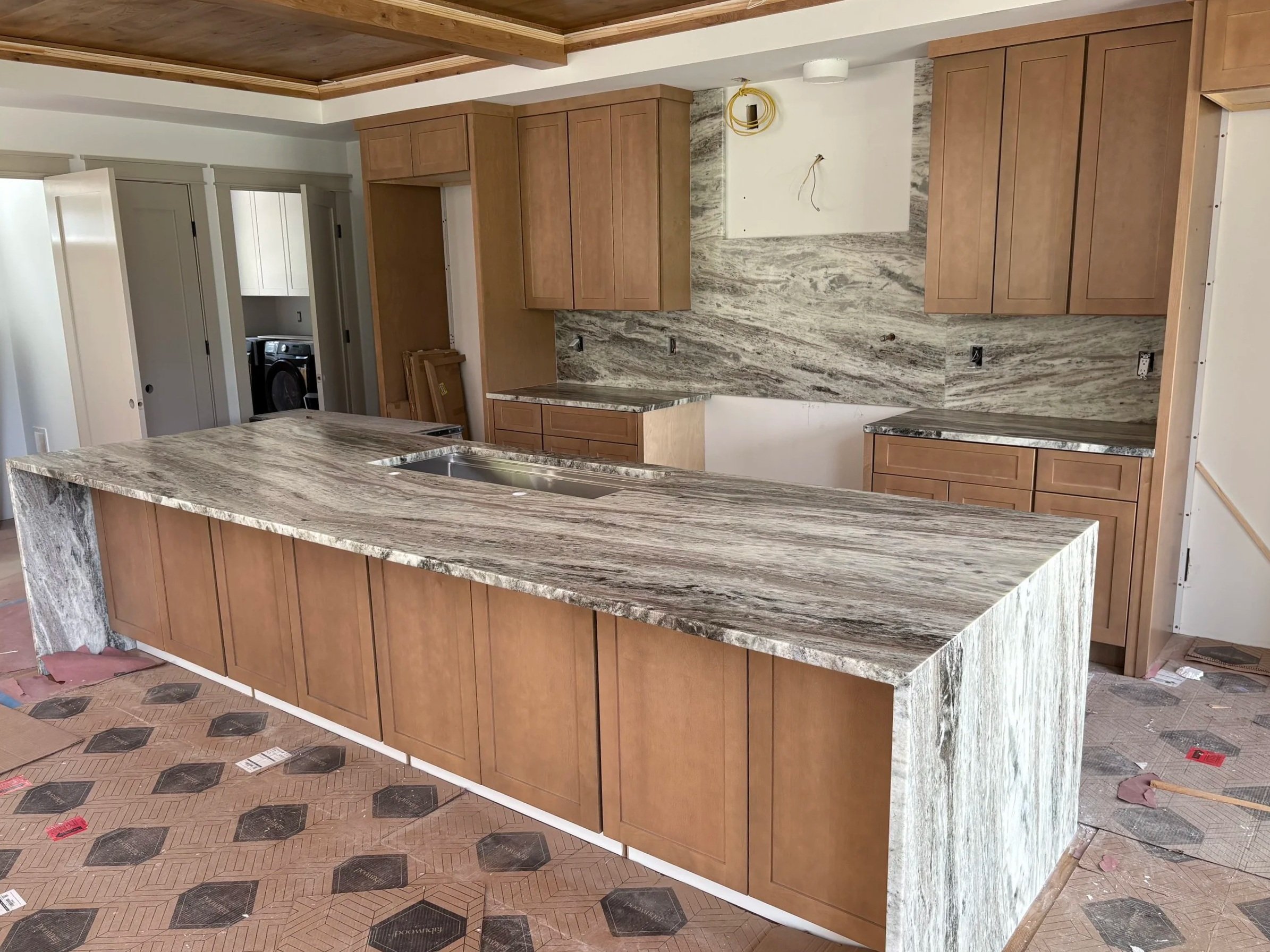 Kitchen under construction with wooden cabinets, granite countertops, and a kitchen island, with construction materials on the floor.