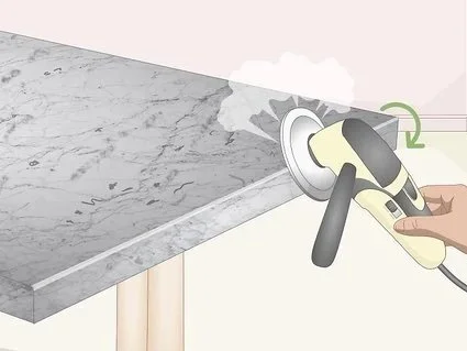 Hand holding a power sander smoothing a marble countertop