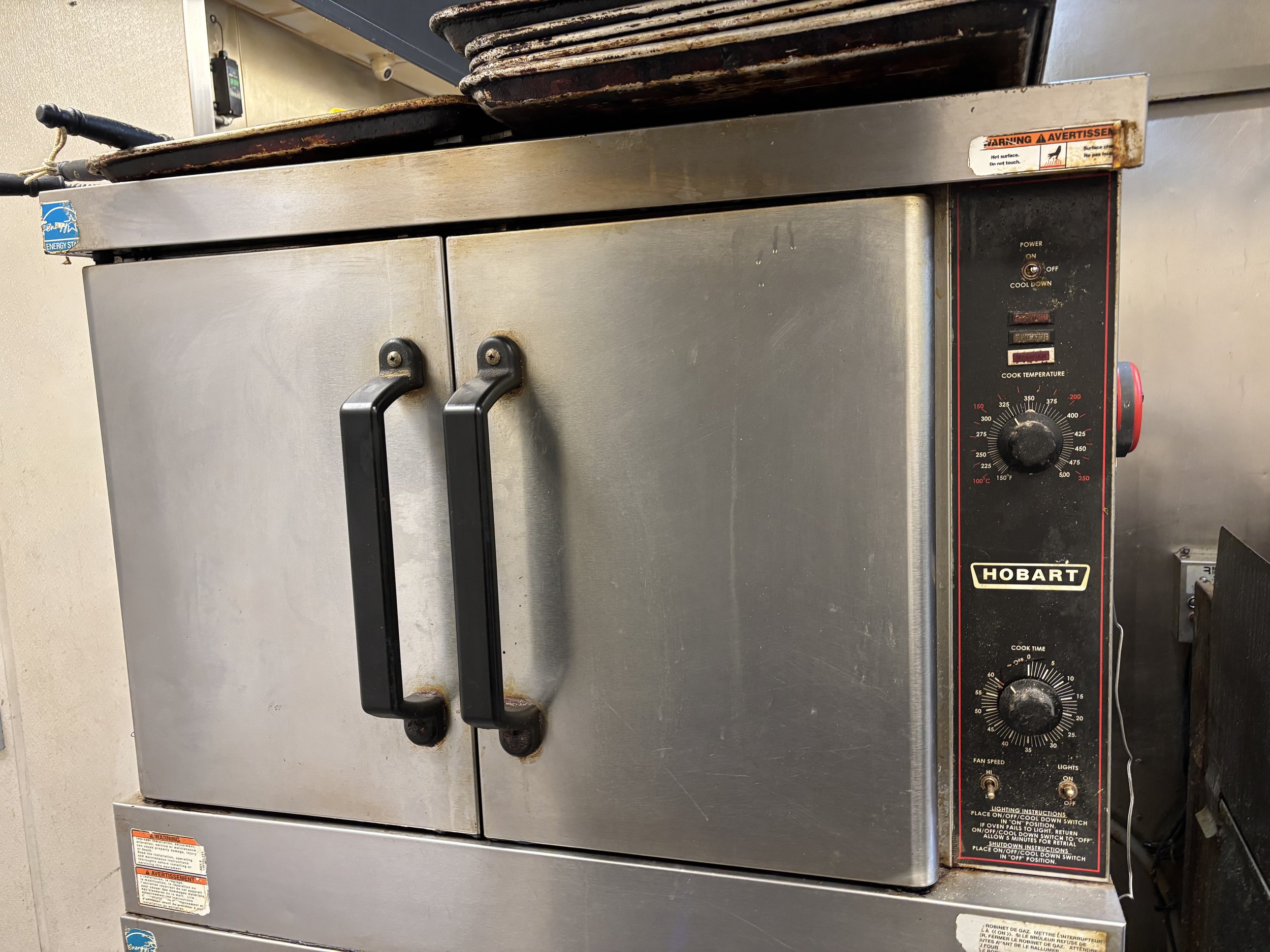 Metal commercial oven with Hobart brand logo and control panel, featuring temperature and timer knobs, in a kitchen setting.